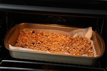 Tasty granola with dried fruits baking in oven, closeup