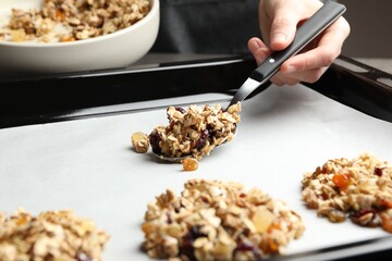 Making granola. Woman putting oat flakes with dried fruits onto tray at table, closeup