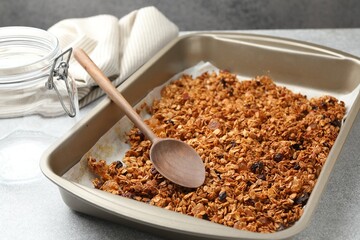 Tasty granola with dried fruits and spoon in tray on light grey table, closeup
