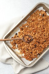 Tasty granola with dried fruits and spoon in tray on light grey table, top view