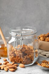 Tasty granola in glass jar and ingredients on light grey table, closeup