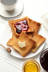 Fresh toasted bread slices served with butter, honey, jam and tea on white wooden table, flat lay