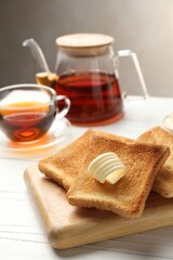 Fresh toasted bread slices served with butter and tea on white wooden table, closeup