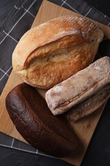 Different types of bread loaves on black table, top view