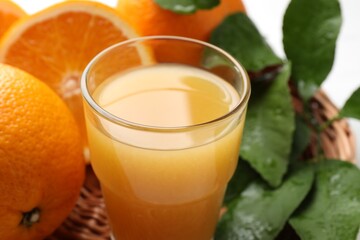 Fresh orange juice, fruits and leaves in basket on white table, closeup
