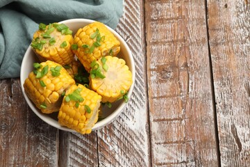 Pieces of boiled corncobs with green onion in bowl on wooden table, top view. Space for text