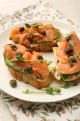 Tasty bruschettas with salmon, avocado, capers and microgreens on light table, closeup