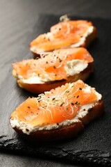 Tasty bruschettas with salmon, cream cheese and microgreens on black table, closeup