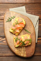 Tasty bruschettas with salmon, arugula and avocado on wooden table, top view