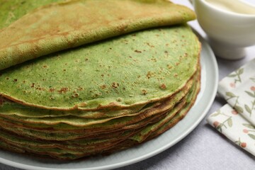 Tasty spinach crepes and sour cream on grey table, closeup