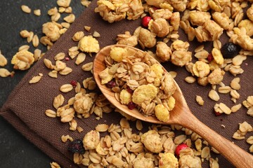 Tasty granola with dried fruits and spoon on black table, top view