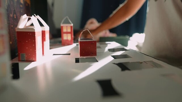 Softly illuminated paper village positioned by gentle human touch
