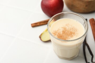 Delicious protein shake in glass, cinnamon, apples and vanilla pods on white tiled table, closeup. Space for text