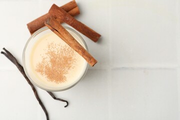 Delicious protein shake in glass, cinnamon and vanilla pods on white tiled table, flat lay. Space for text