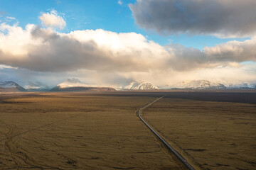 Drone view of long road in northeastern Iceland amidst volcanic landscapes. Dramatic sky, mountains.