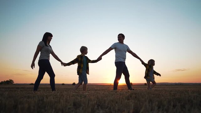 Family walking holding hands at sunset across golden field with father and mother leading child and children in silhouette stride joyful family connection and playful child running in sunset glow