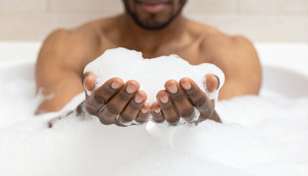 A person holding a large amount of white bath foam in their cupped hands while relaxing in a bathtub. - Powered by Adobe