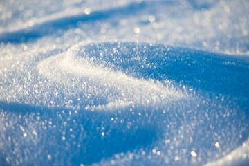 Deeply frozen snow surface with wavy structures created by wind drifts on a sunny winter morning in the Sauerland region (Germany). Christmassy background  with glittering ice crystals and snowflakes.