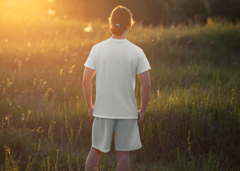 Template of a white t-shirt, shorts on a long-haired man, back view, casual suit on the background of nature, sunset, rustic.