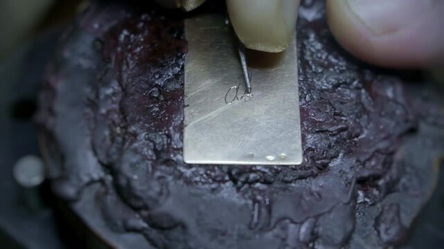 Hand engraving elegant cursive script letters into gold jewelry pendant closeup macro detail