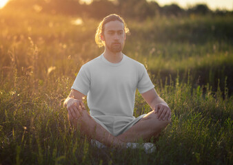 Mockup of white t-shirt, shorts on long-haired bearded man, front view, sitting in field on sunset background.