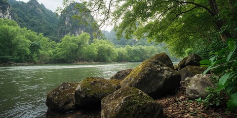 Large moss-covered rocks on a riverbank with grass and trees, showcasing natural erosion and seasonal change