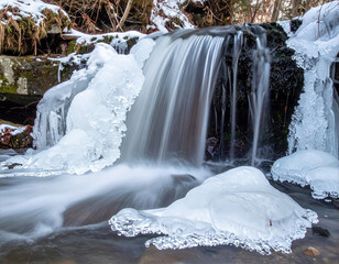 Partially frozen waterfall with silky flowing water and blue ice in a snowy forest scene