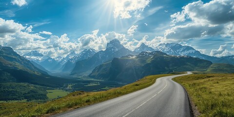 A scenic mountain landscape with a curving road winding through vibrant green terrain and snow-covered summits, ideal for outdoor activities