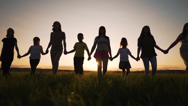 people holding hand at sunset in field of tall grass showing silhouette of family woman girl child standing together across horizon with warm light and unity and intergenerational connection near glow