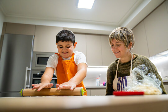 Mother and son enjoying baking, preparing dough with a rolling pin in a modern home kitchen, fostering family bonding - Powered by Adobe
