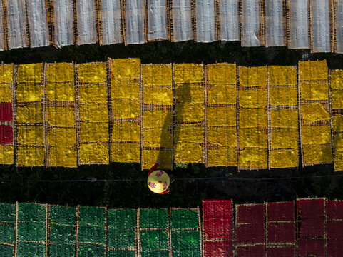 Aerial view of a person in traditional conical hat walks amid vibrant trays of colorful drying goods, creating a striking mosaic under the sun, Tay Ninh, Tay Ninh, Vietnam.