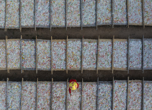 Aerial view of a person walking between drying rice paper sheets, creating a textured pattern of white, red, and yellow dots, Tay Ninh, Tay Ninh, Vietnam.