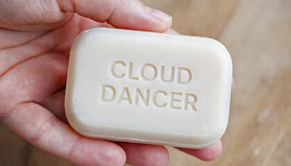 Caucasian woman holding a bar of natural handmade soap with embossed cloud dancer text. Organic skincare product for washing and bathing.