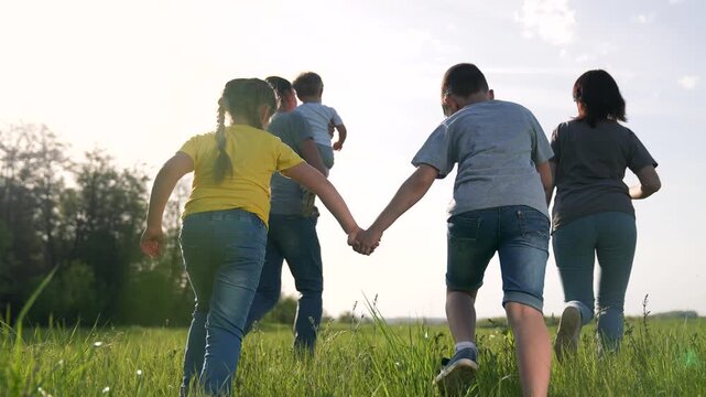 Walking family through green field holding hands while parent carries child and others walk together in tall grass under bright sky and distant tree line sunny summer afternoon showing family bond