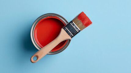 Open can of red paint with brush on light blue background. Flat lay composition for renovation, wall painting, and home improvement advertising.