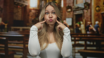Woman pressing cheeks with index fingers to pull a funny face in church; fun playfulness humor silliness.
