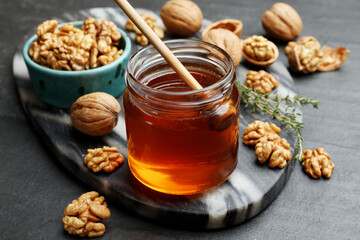 Delicious honey in glass jar, dipper, walnuts and thyme on dark textured table, closeup