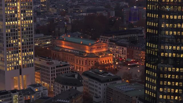Aerial night view of historic Alte Oper concert hall in Frankfurt am Main, Germany. Illuminated building nestled between modern high rise office towers