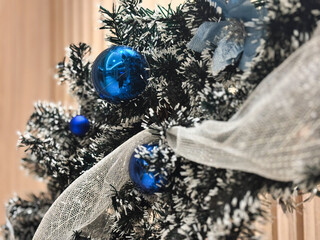 A close-up, selective focus shot of a snowy or flocked Christmas wreath or tree detail. The dark green faux pine needles are heavily dusted with white flocking, creating a frosty winter effect.