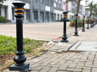 A row of decorative, black metal bollards with distinct yellow-orange bands lining a paved pedestrian walkway or sidewalk.