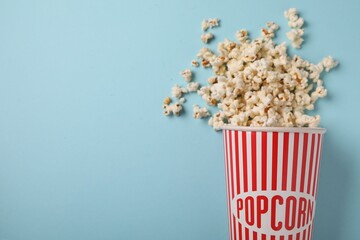 Fresh tasty popcorn and paper cup on light blue background, flat lay. Space for text