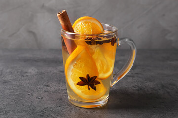 Delicious mulled white wine with slices of orange and spices in glass cup on dark textured table against grey background, closeup