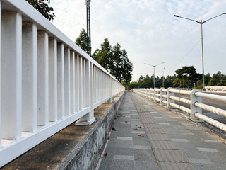 A low-angle, eye-level perspective shot of a clean, modern white metal barrier or railing running along the edge of an elevated roadside pedestrian walkway (sidewalk).