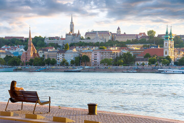 Relaxed woman sitting on a bench against river and old city