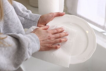 Woman wiping plate with paper towel in kitchen, closeup