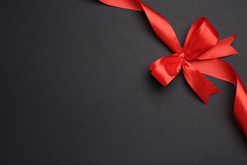 Beautiful red ribbon with bow on dark background, top view. Space for text