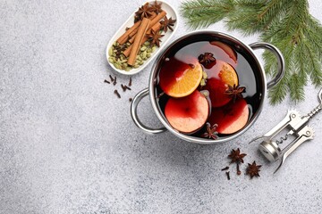 Traditional mulled wine in pot, corkscrew, spices and fir tree branches on light grey table, flat lay. Space for text