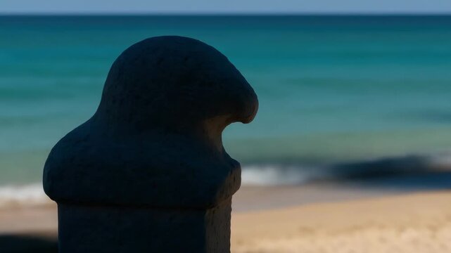 Stone bollard by the ocean with shifting sunlight on sandy beach