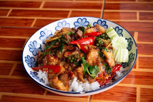 Pad Cha Moo Krob (spicy stir-fried crispy pork belly) served over white rice. The dish is vibrant with chili, basil, peppercorns, and other Thai herbs, showcasing a rich, savory, and spicy flavor. 