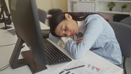 Woman resting head on desk at computer monitor and keyboard, hand to face gesture in an office...